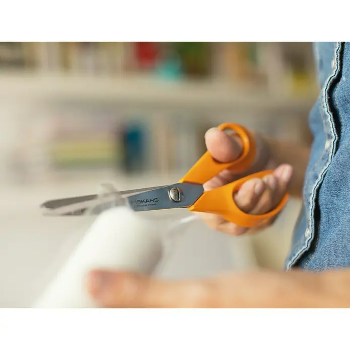 Fiskars Universalschere Classic - Länge: 21 cm - Nahaufnahme einer Hand, die eine orangefarbene Fiskars-Schere hält und etwas zuschneidet, wahrscheinlich ein Bastelprojekt.