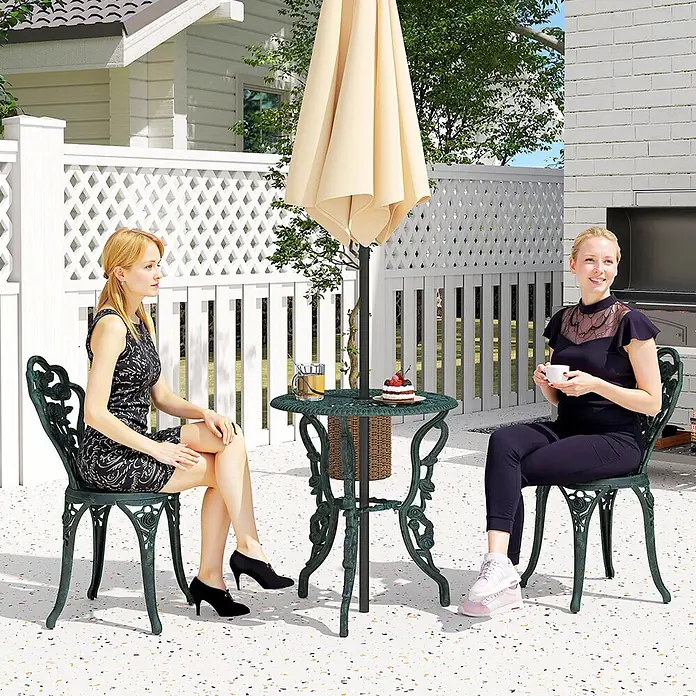 Outsunny Gartenstuhl-Set mit Schirmhalterung - 2 Stk., Gussaluminium, Gusseisen, Antik-Grün, B x T x H: 60 x 60 x 69 cm - Zwei Frauen sitzen an einem dunkelgrünen Bistro-Set aus Gusseisen mit verzierten Stühlen und einem Tisch unter einem Sonnenschirm auf einer Terrasse.