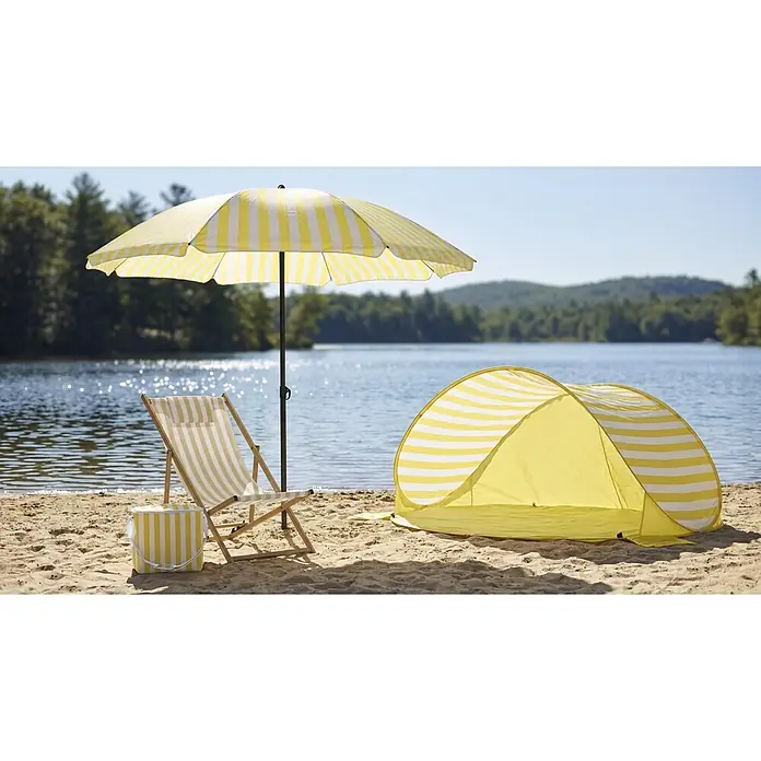 Strandschirm - Weiß/Gelb, Durchmesser Bespannung: 180 cm - Gelb-weiß gestreifter Sonnenschirm, Liegestuhl, Kühltasche und Strandmuschel am sandigen Seeufer.