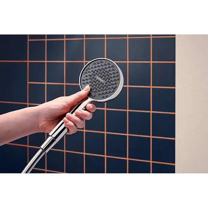 Hansgrohe Set de ducha Activera - Número de tipos de chorro: 2 ud., Cromo - Una mano sostiene una ducha de mano Hansgrohe cromada con una placa rociadora gris oscuro frente a una pared de azulejos.