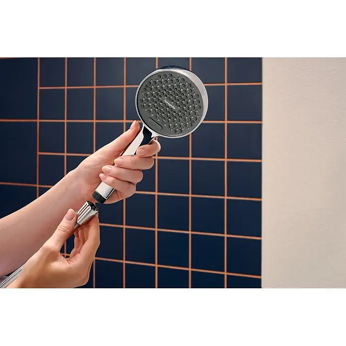 Hansgrohe Teleducha Activera Select S - Diámetro: 9,5 cm, Cromo - Manos ensamblando un cabezal de ducha cromado con una cara rociadora gris oscuro y una manguera de ducha cromada contra una pared de azulejos azules.