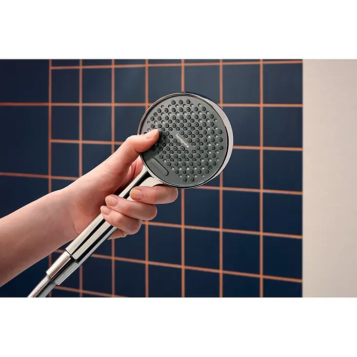 Hansgrohe Teleducha Activera Select S - Diámetro: 9,5 cm, Cromo - Una mano sostiene un cabezal de ducha cromado con una placa de boquillas gris oscuro frente a una pared de azulejos.