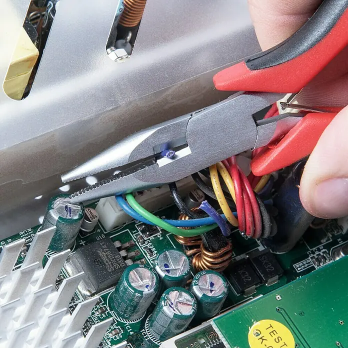 Connex Alicates planos - Largo: 12 cm - Un primer plano de reparación electrónica con alicates trabajando en cables de colores, sobre un circuito verde.