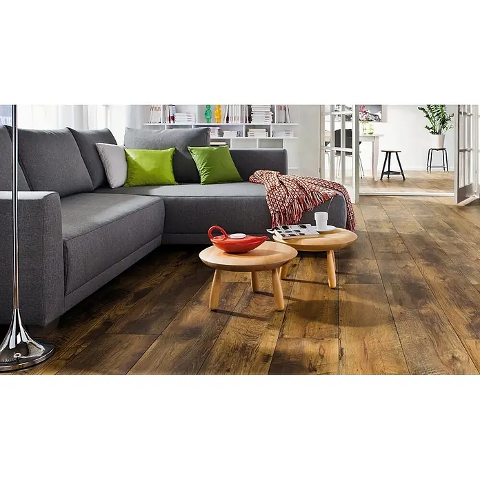 Living by Haro Laminat Gigante - Eiche Fattoria, Landhausdiele, 2.200 x 243 x 8 mm - Dunkler Laminatboden in Holzoptik in einem modernen Wohnzimmer mit grauem Sofa und Holztischen.