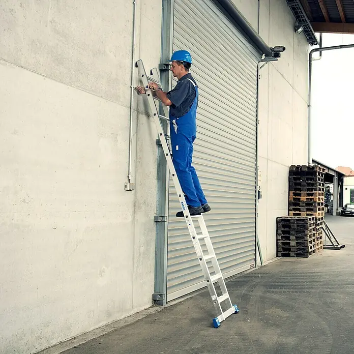 Krause Stabilo Anlegeleiter + S - Anzahl Tritte: 12 Stk., Arbeitshöhe: 4,1 m, Aluminium - Ein Arbeiter benutzt eine KRAUSE Vielzweckleiter, um an einer Wand zu arbeiten, was die Vielseitigkeit und den Komfort der Leiter hervorhebt.