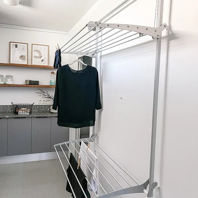 Foxydry Wandwäschetrockner Wall Plus 100 Weiß - 108 cm, Farbe: Weiß - Wandmontierter, grauer Metallwäscheständer mit zwei Ebenen, beladen mit schwarzer und weißer Wäsche in einem modernen Waschraum.