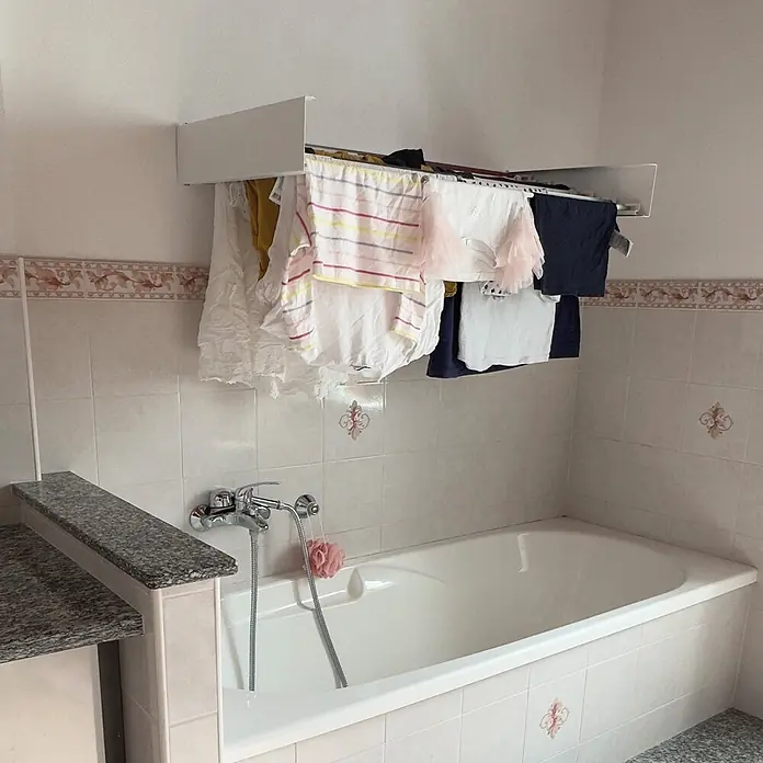 Foxydry Wandwäschetrockner Hide 100 Weiß - 101 cm, Farbe: Weiß - Weißer, wandmontierter Wäschetrockner über einer Badewanne, der verschiedene Kleidungsstücke zum Trocknen hält.
