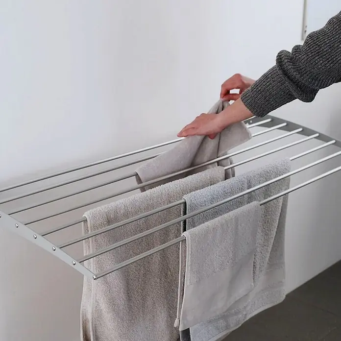 Foxydry Wandwäschetrockner Down 80 Grau - 82 cm, Farbe: Stahlgrau - Hände legen ein hellgraues Handtuch auf einen grauen, wandmontierten Wäscheständer mit weiteren Handtüchern.