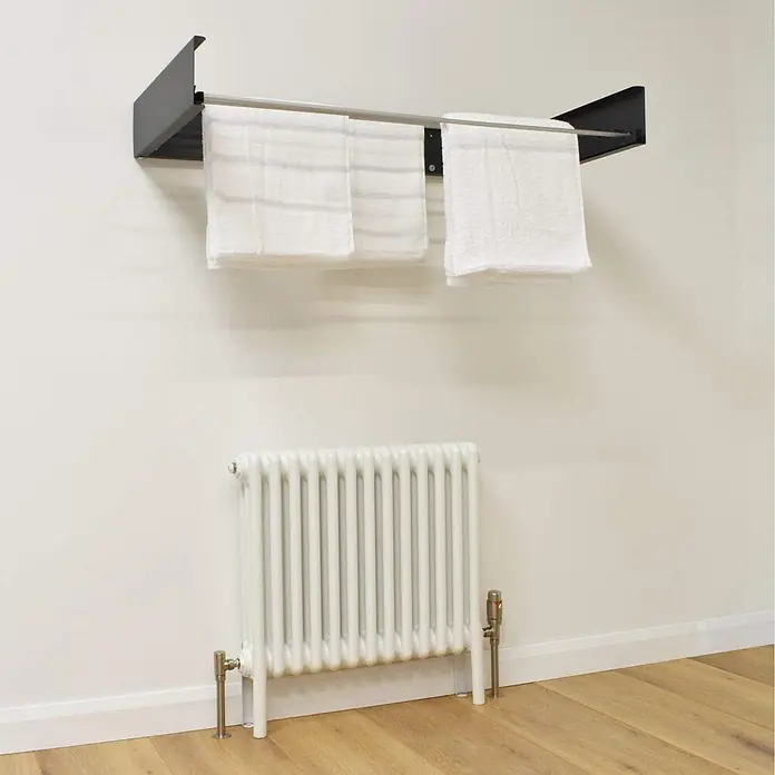 Foxydry Wandwäschetrockner Hide 70 Anthrazit - 71 cm, Farbe: Anthrazitschwarz - Schwarzer Regal-Handtuchwärmer mit silberner Stange, hält weiße Handtücher, über weißem Heizkörper an der Wand.