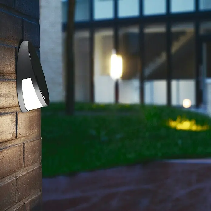 Lutec Aplique exterior LED Sandwy - 9 W, 7 x 18,6 x 18,6 cm, Antracita/Blanco, Opal, IP44 - Una elegante lámpara de pared exterior con iluminación LED montada en una pared de ladrillo, que muestra un diseño moderno y elegante.