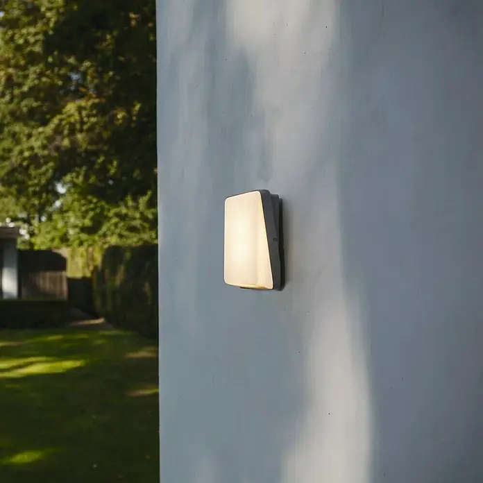 Lutec Aplique exterior LED Even - 15 W, 4,5 cm x 18,5 cm x 19 mm, Gris, IP54 - Esta imagen captura una lámpara de pared rectangular con estilo que emite un brillo cálido, perfecta para crear un ambiente acogedor.