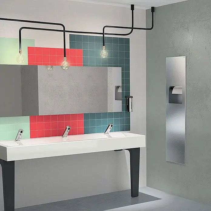 Delabie Spültischarmatur Delabie - Chrom - Langes, weißes Waschbecken mit drei integrierten Chromarmaturen und schwarzen Beinen in einem modernen öffentlichen Waschraum.