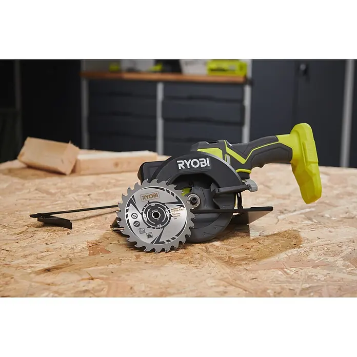 Ryobi ONE+ Akku-Handkreissäge R18CS115 - 18 V, Ohne Akku, Durchmesser Sägeblatt: 115 mm, 5.200 U/min - Eine schwarz-gelbe Ryobi Kreissäge mit silbernem Sägeblatt liegt auf einer OSB-Werkbank in einer Werkstatt.