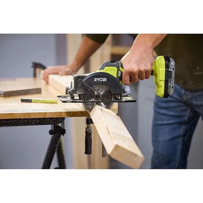 Ryobi ONE+ Akku-Handkreissäge R18CS115 - 18 V, Ohne Akku, Durchmesser Sägeblatt: 115 mm, 5.200 U/min - Eine Person nutzt eine lindgrüne und schwarze Ryobi Akku-Kreissäge zum Schneiden eines Holzbretts, Sägemehl ist sichtbar.