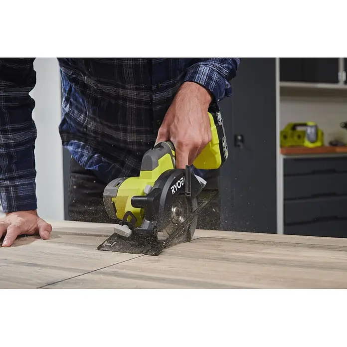 Ryobi ONE+ Akku-Handkreissäge R18CS115 - 18 V, Ohne Akku, Durchmesser Sägeblatt: 115 mm, 5.200 U/min - Eine Person sägt mit einer grün-schwarzen Akku-Kreissäge ein helles Holzbrett, wobei Späne entstehen.