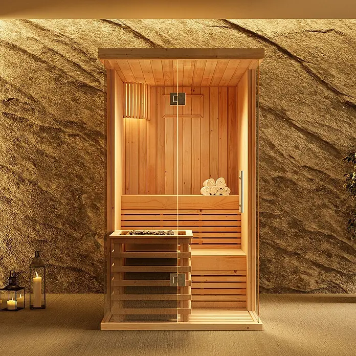 FinnTherm Massivholzsauna Milla -  - Moderne Holzsauna mit Glasfront, Innenheizung und Handtüchern, vor einer Steinwand mit Ambientebeleuchtung und Kerzen.