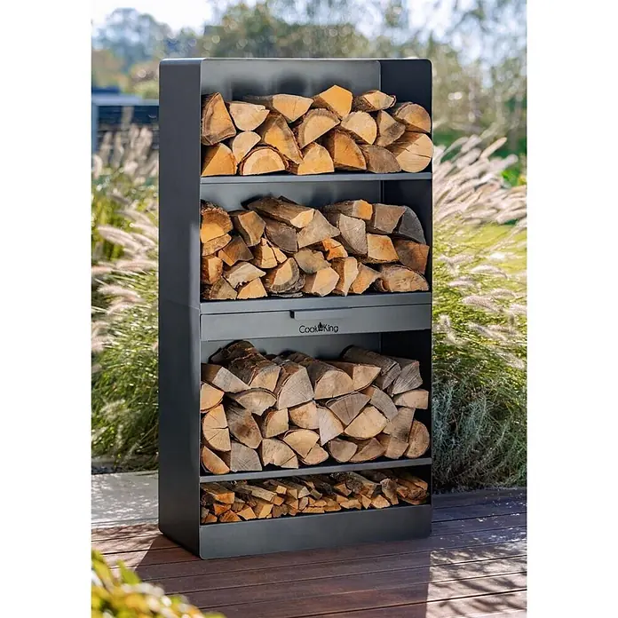 Bene on Fire Kaminholzregal Oregon - 30 x 30 x 120 cm, Stahl, schwarz - Dunkelgraues Metall-Kaminholzregal von CookKing mit vier Fächern, gefüllt mit Brennholz, im Freien.