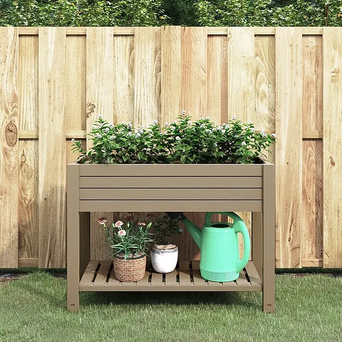 Furnicato Hochbeet - 110 x 45 x 79 cm, Kunststoff, Hellbraun - Ein taupefarbenes Hochbeet mit Latten-Pflanzkasten oben und einer unteren Ablage mit Topfpflanzen und einer Gießkanne, in einem Garten vor einem Holzzaun.