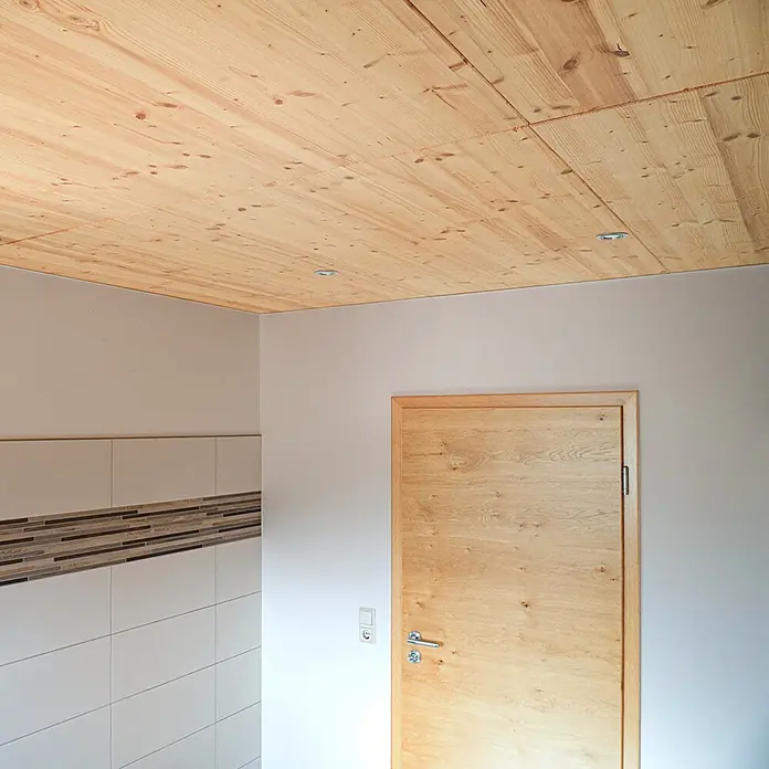 elka 3-Schichtplatte Vita - Douglasie, 2.500 x 660 x 19 mm - Helle Holzdeckenpaneele mit sichtbarer Maserung und Ästen, beleuchtet durch Einbaustrahler.