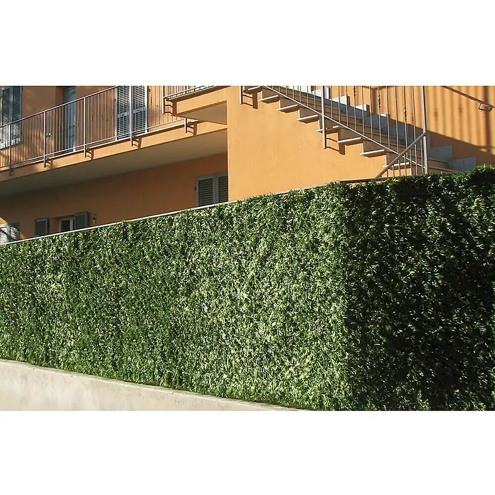 Ocultación Seto Artificial Extra - Verde, L x Al: 3 x 1 m - Primer plano de un seto artificial frente a un edificio, que proporciona privacidad y verdor. Ideal para decorar espacios exteriores.