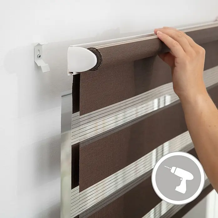 Lichtblick Doppelrollo -  - Braunes und weißes gestreiftes Duo-Rollo wird an Wand montiert; Hand hält Mechanismus, Halterung und Bohrmaschinen-Icon sind sichtbar.