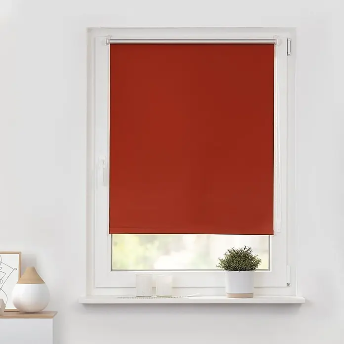 Lichtblick Thermorollo - Terracotta - Rotes Rollo, in einem weißen Fensterrahmen montiert und teilweise heruntergelassen.