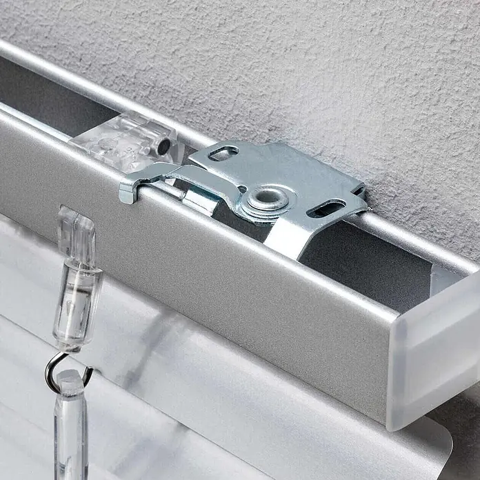 Lichtblick Jalousie - Silber, Aluminium - Silberne Aluminium-Jalousiekopfschiene mit Metallhalterungen an einer Wand befestigt, mit transparenten Kunststoffclips für die Jalousielamellen.