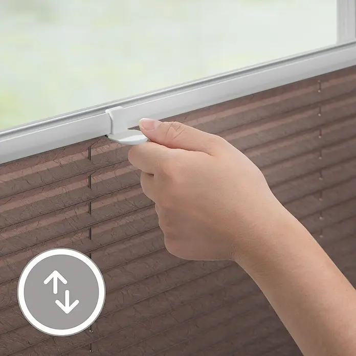 Lichtblick Plissee - Taupe - Hand justiert ein braunes Plissee mit weißem Griff am Fenster.