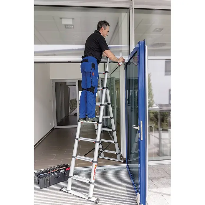 Munk Teleskopleiter Teleskop-Kombileiter Combi Line - Anzahl Tritte: 8 Stk., Arbeitshöhe: 3.500 m - Silberne Aluminium-Mehrzweckleiter, von einem Mann zum Arbeiten an einem blauen Türrahmen verwendet.