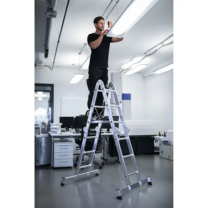 Munk Mehrzweckleiter Vielzweckleiter mit Nivello® Traverse 4x4 Sprossen - Anzahl Tritte: 4 Stk., Arbeitshöhe: 5.850 m, Aluminium - Mann auf einer silbernen Mehrzweckleiter installiert eine Deckenleuchte im Büro.