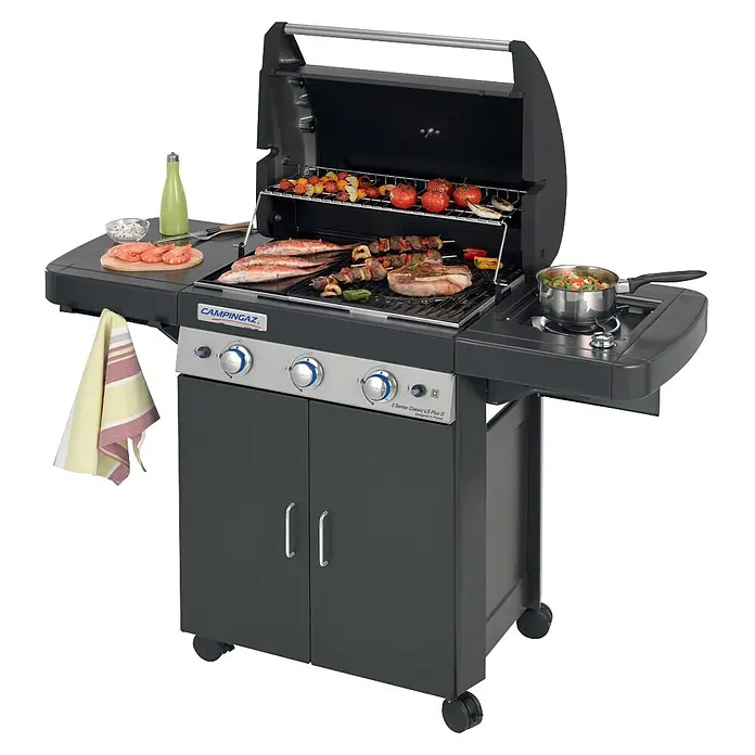 Campingaz Barbacoa de gas Classic LS Plus - Superficie de la parrilla (An x Pr): 61 x 45 cm, 3,2 kW, Número de quemadores: 3 - Parrilla de gas Campingaz gris oscuro con comida cocinándose en las rejillas y quemador lateral, y armario.