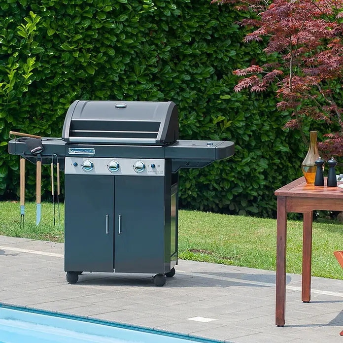 Campingaz Barbacoa de gas Classic LS Plus - Superficie de la parrilla (An x Pr): 61 x 45 cm, 3,2 kW, Número de quemadores: 3 - Barbacoa de gas gris con utensilios de cocina en un patio junto a una piscina, lista para asar al aire libre.