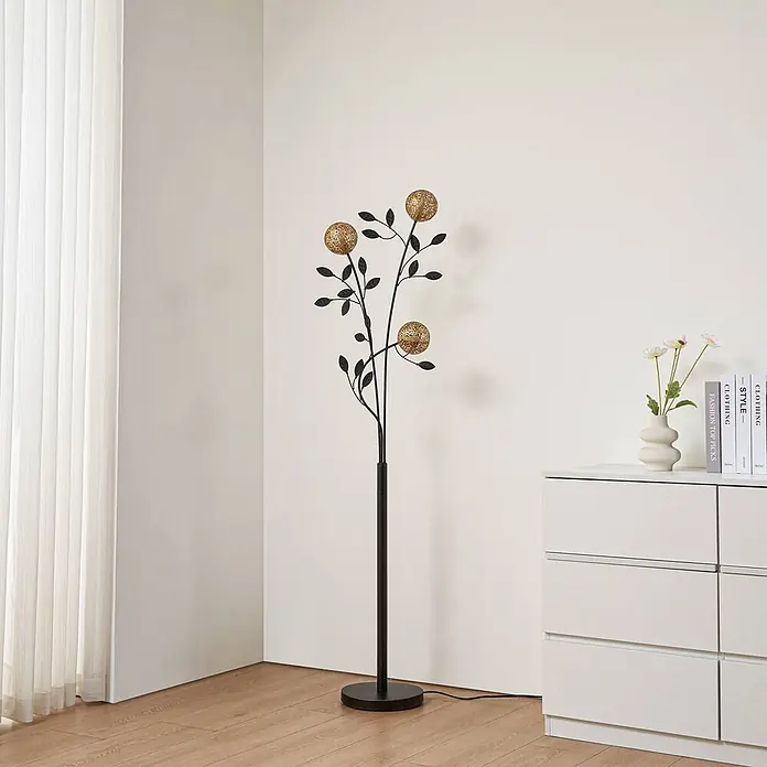 Lucande Stehleuchte Evory - schwarz, messing / gold, G9 - Eine hohe Stehlampe mit schwarzem, baumartigem Ständer und drei glitzernden goldenen Kugelleuchten in einem modernen Wohnzimmer.