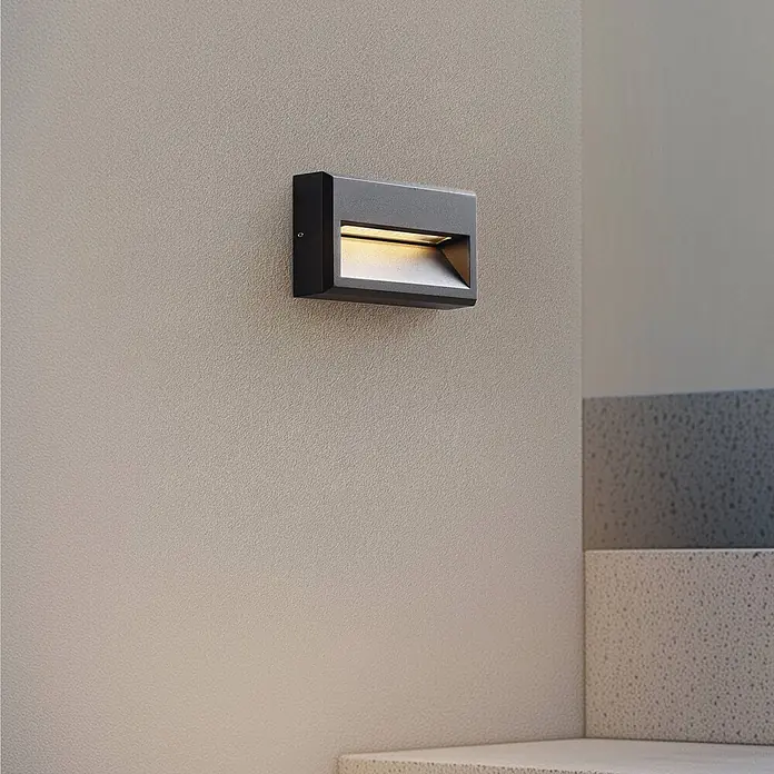 Lucande Außenwandleuchte Weno - 3,5 x 22,7 x 12,7 cm, schwarz, IP65 - Anthrazitfarbene rechteckige Wandleuchte an einer strukturierten Wand, die ein warmes Licht nach unten wirft, ideal für Treppen oder Flure.