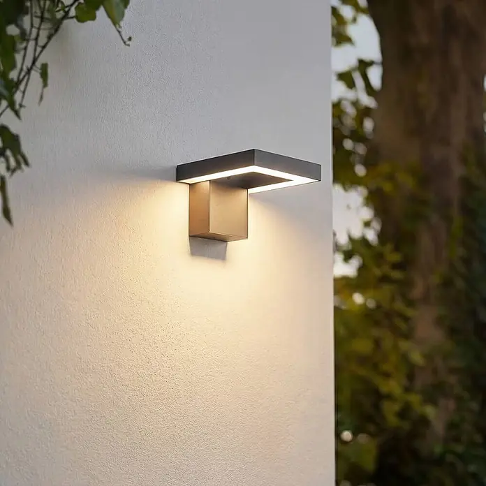 Lindby Außenwandleuchte Orbin - alu / grau / zink, IP54 - Moderne anthrazitfarbene quadratische Außenwandleuchte, die warmes Licht auf eine strukturierte Wand abgibt.