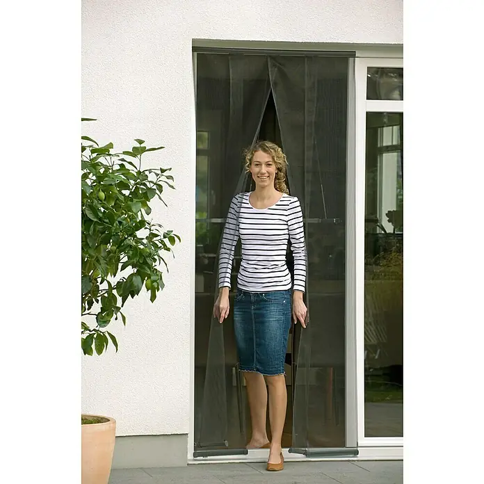 Tesa Insect Stop Mosquitera Standard - An x Al: 95 x 220 cm, Montaje de la mosquitera: Enganche, Antracita - Mujer pasa por una puerta mosquitera magnética que se cierra automáticamente e impide la entrada de insectos.