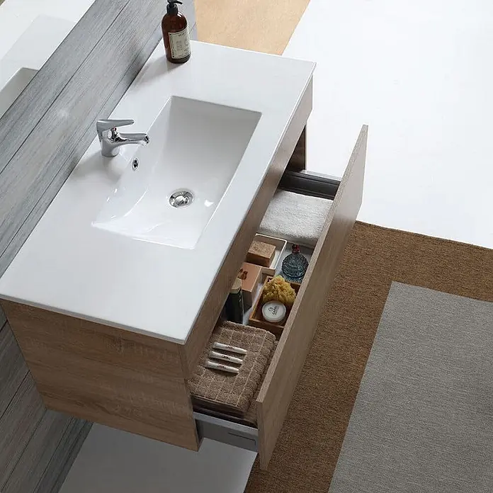 Kiamami Valentina Badmöbel-Set - Helles Holz - Badezimmerschrank aus hellem Holz mit integriertem weißen Waschbecken und offener Schublade, gefüllt mit Toilettenartikeln und Handtüchern.