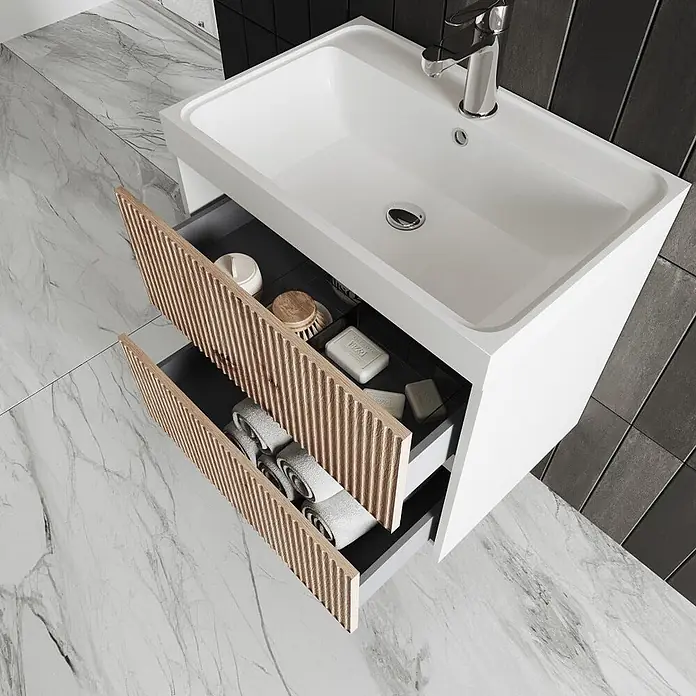 Kiamami Valentina Badmöbel-Set - Braun - Weißer Badunterschrank mit integriertem Waschbecken und zwei offenen Schubladen mit Holzlamellenfronten, die Toilettenartikel und gerollte Handtücher zeigen.