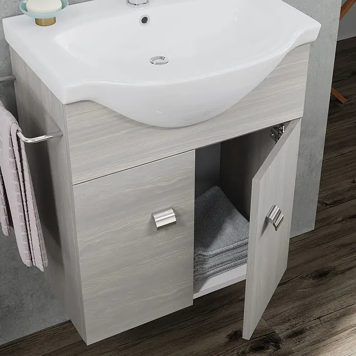 Kiamami Valentina Badmöbel-Set - Grau - Ein Badezimmerwaschtisch in heller Holzmaserung mit weißem Keramikwaschbecken und Chromgriffen, im Badezimmer mit Handtüchern.