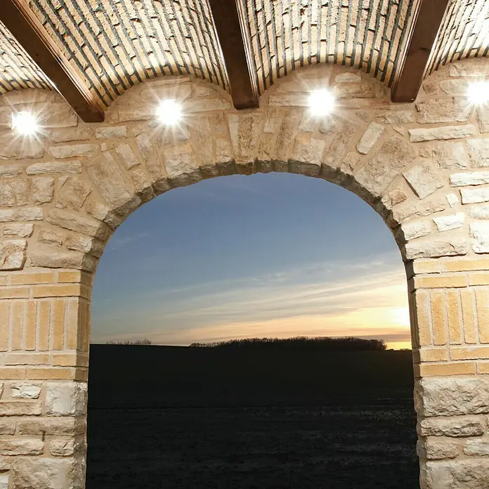 Esquina exterior Silleria Cobre - Cantidad total: 9 pzs. - Arco de piedra que enmarca un paisaje al atardecer, realzado con iluminación empotrada. La mampostería acentúa la belleza natural.