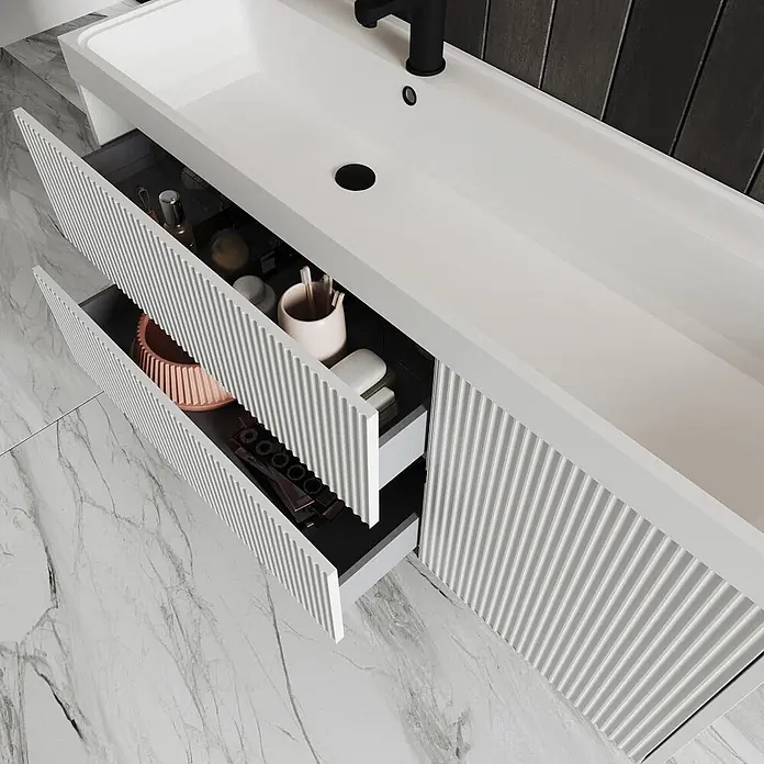 Kiamami Valentina Badmöbel-Set - Weiß - Weißer Badezimmerschrank mit gerippter Front, integriertem Waschbecken und zwei geöffneten Schubladen mit Toilettenartikeln.