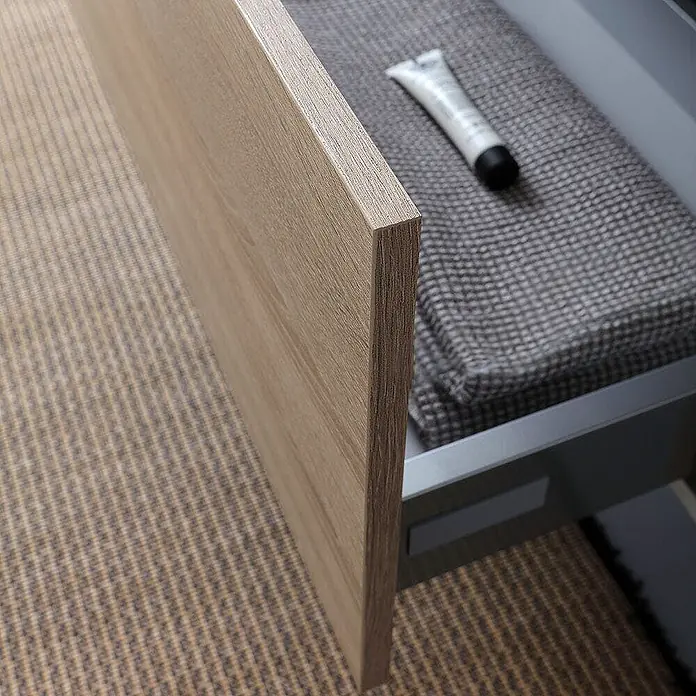 Kiamami Valentina Badmöbel-Set - Helles Holz - Teilweise geöffnete Schubladenfront aus hellem Holz, die einen grauen Innenraum mit einem grauen Handtuch und einer weißen Tube zeigt.