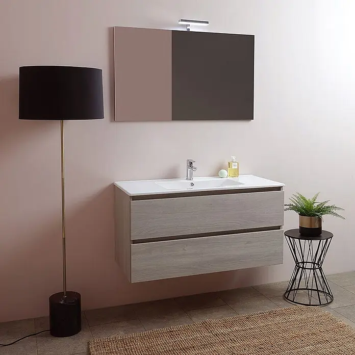 Kiamami Valentina Badmöbel-Set - Helles Holz - Heller Holz-Badezimmerschrank mit weißem Waschbecken, unter einem Spiegel mit Licht, in einem modernen Badezimmer.