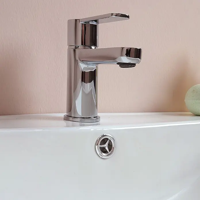 Kiamami Valentina Badmöbel-Set - Helles Holz - Moderner Chrom-Wasserhahn auf einem weißen Keramikwaschbecken, mit sichtbarem Überlauf.
