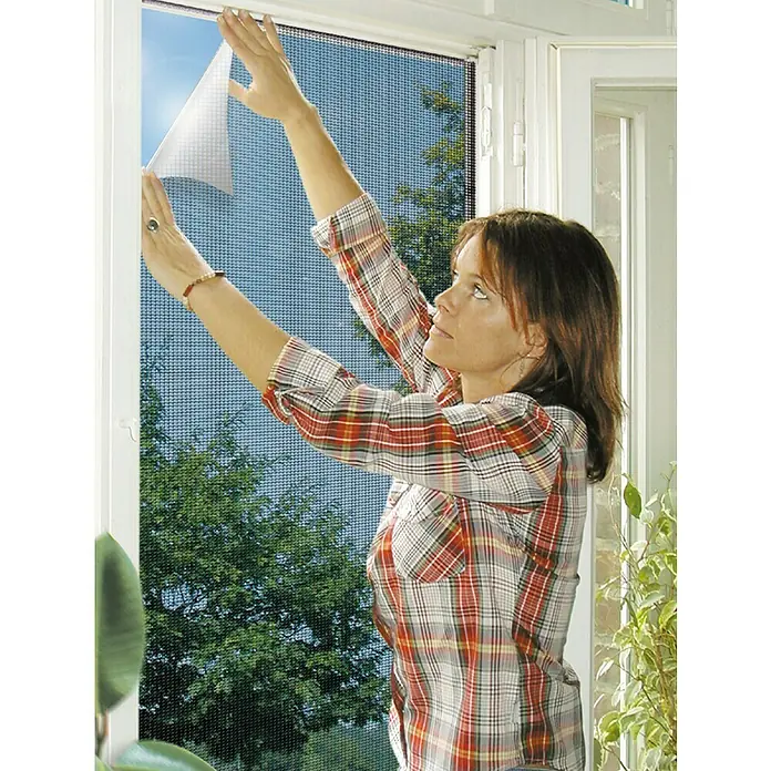 Schellenberg Insect Stop Mosquitera Reflection - An x Al: 150 x 130 cm, Montaje de la mosquitera: Pinzas - Una mujer instalando una mosquitera en una ventana. El producto protege contra insectos y garantiza la circulación de aire fresco.
