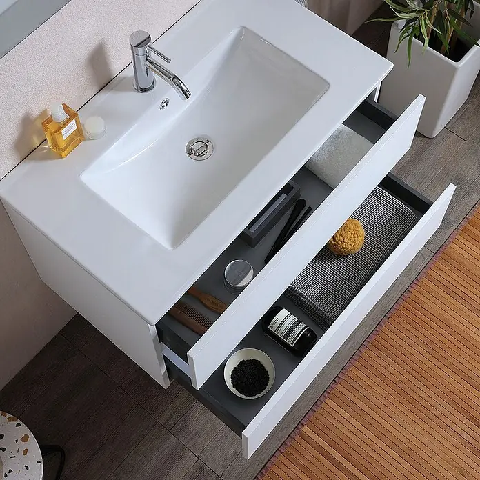 Kiamami Valentina Badmöbel-Set - Weiß - Weißer wandmontierter Badezimmerunterschrank mit integriertem Waschbecken und zwei offenen grauen Schubladen mit Toilettenartikeln.