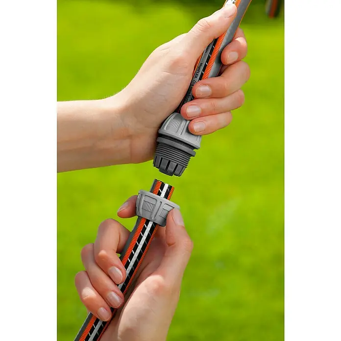 Gardena Reparador de manguera 13-15 mm - Ámbito de uso: Riego - Manos conectan dos partes de manguera de jardín con un conector Gardena delante de un fondo verde.