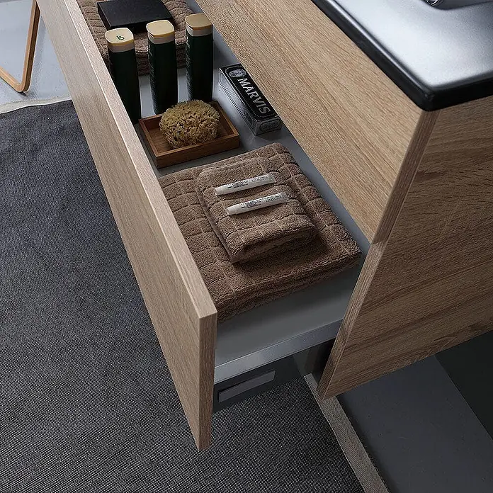Kiamami Valentina Badmöbel-Set - Helles Holz - Offene Badezimmerschublade aus hellem Holz mit ordentlich arrangierten Handtüchern, Pflegeprodukten und einem Naturschwamm.