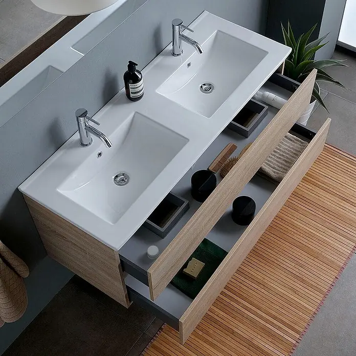 Kiamami Valentina Badmöbel-Set - Braun - Doppelwaschtisch aus hellem Holz mit weißen Keramikbecken und Chromarmaturen. Geöffnete Schubladen zeigen Badartikel.