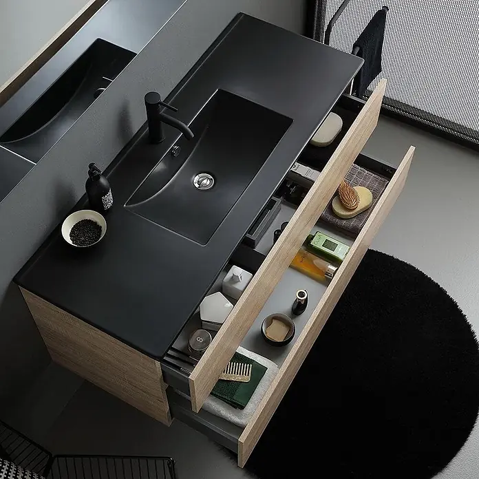 Kiamami Valentina Badmöbel-Set - Braun - Moderne Badmöbel mit integriertem schwarzem Waschbecken und Arbeitsplatte, zwei offene helle Holzschubladen zeigen Toilettenartikel.